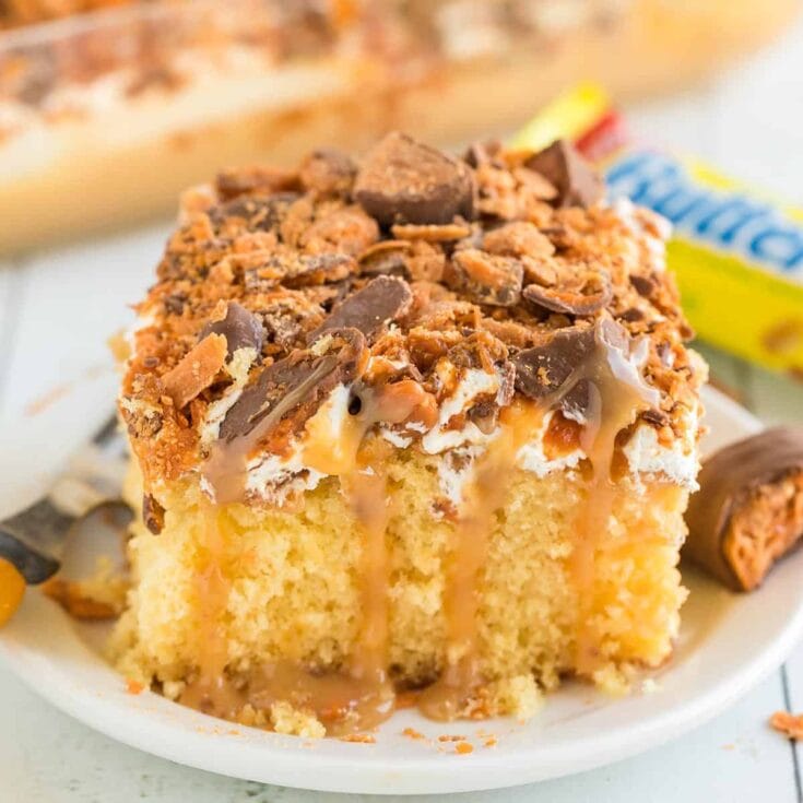 Butterfinger cake slice topped with candy and caramel drizzle.