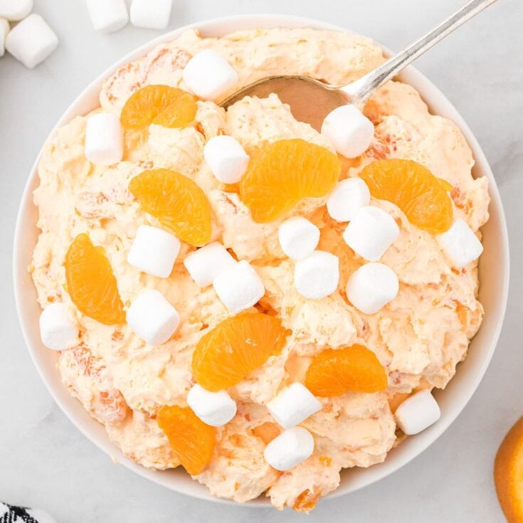Orange fluff salad topped with mandarin oranges and mini marshmallows in a white bowl.