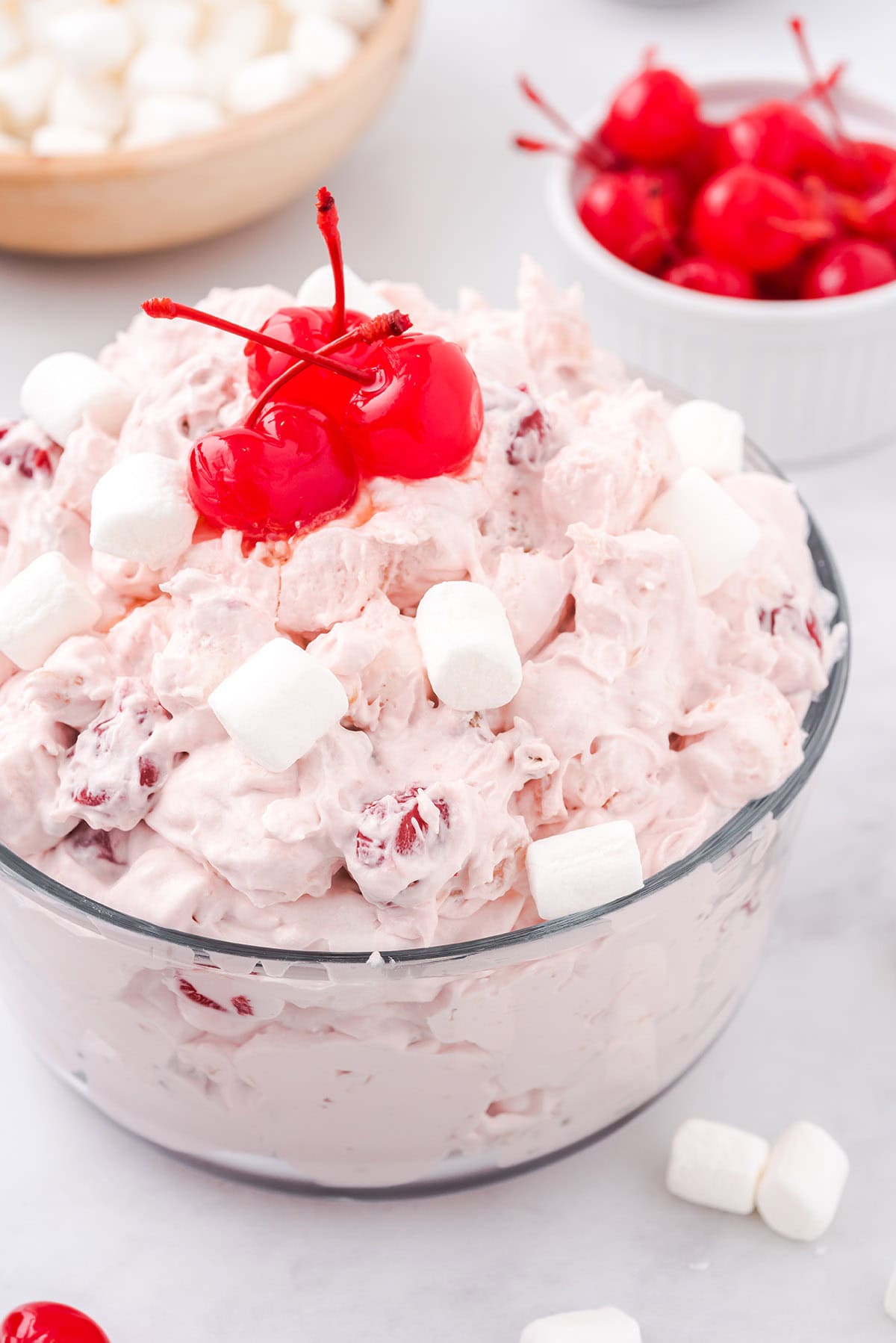 A glass bowl of cherry fluff dessert topped with bright maraschino cherries and mini marshmallows.