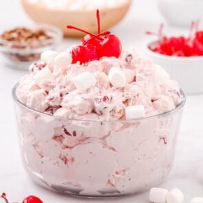 A bowl of cherry fluff dessert topped with maraschino cherries and mini marshmallows.