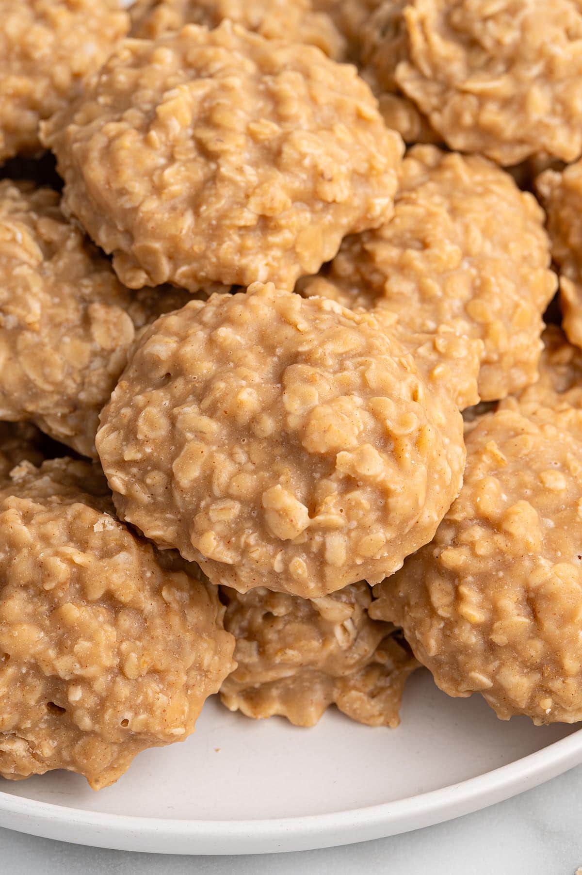 Stacked no-bake peanut butter oatmeal cookies on a white plate, showing their soft texture and rich, nutty color up close.