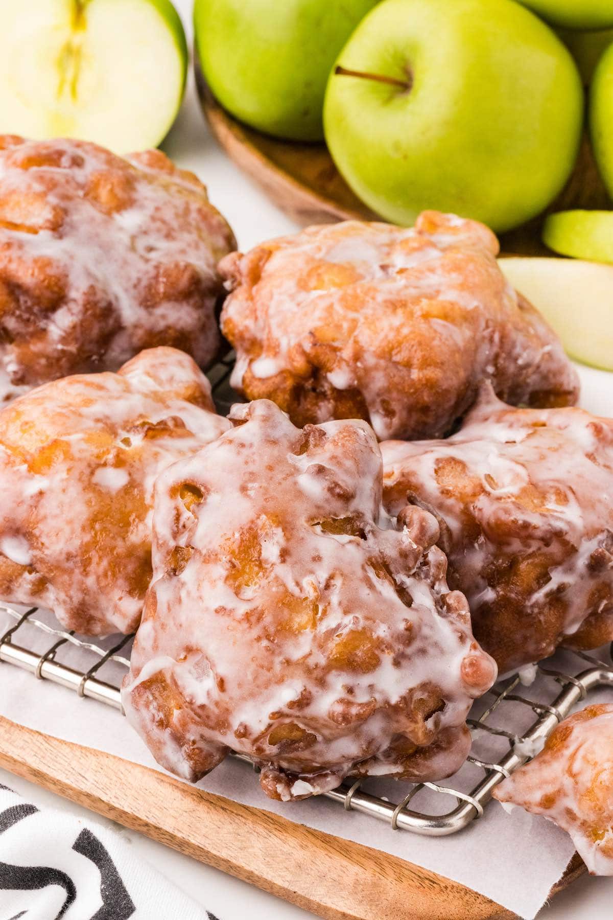 apple fritters with glaze stacked on top of wooden board. 