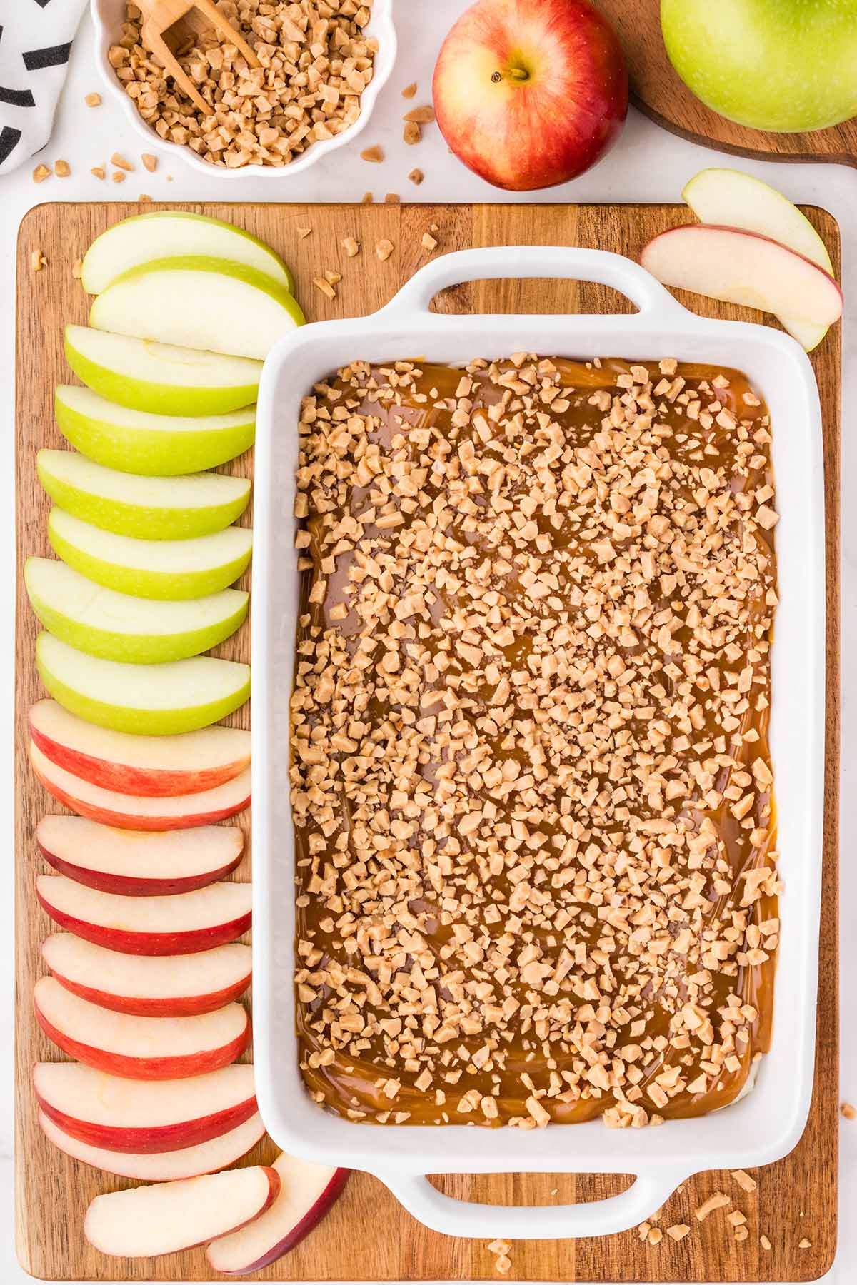 caramel apple dip served on top of wooden board and a couple of apple slices. 