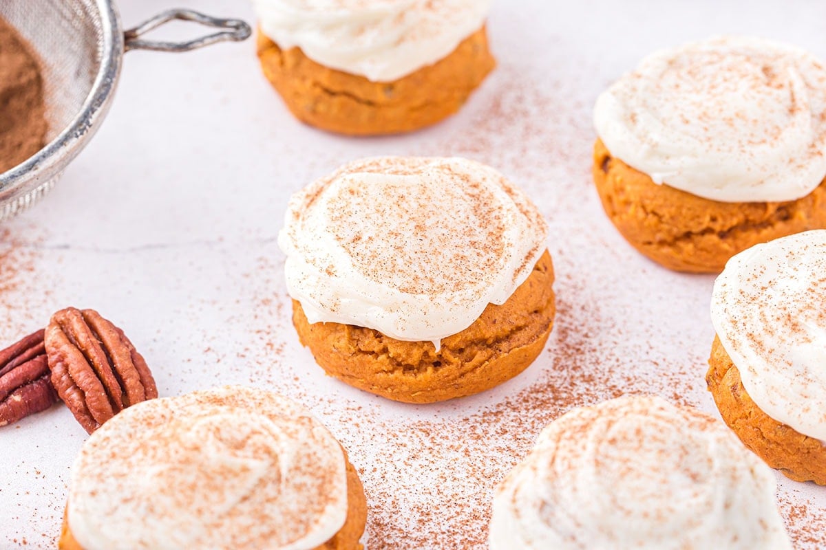 Pumpkin Cake Mix Cookies on the table with white frosting on top and dusted with spice.