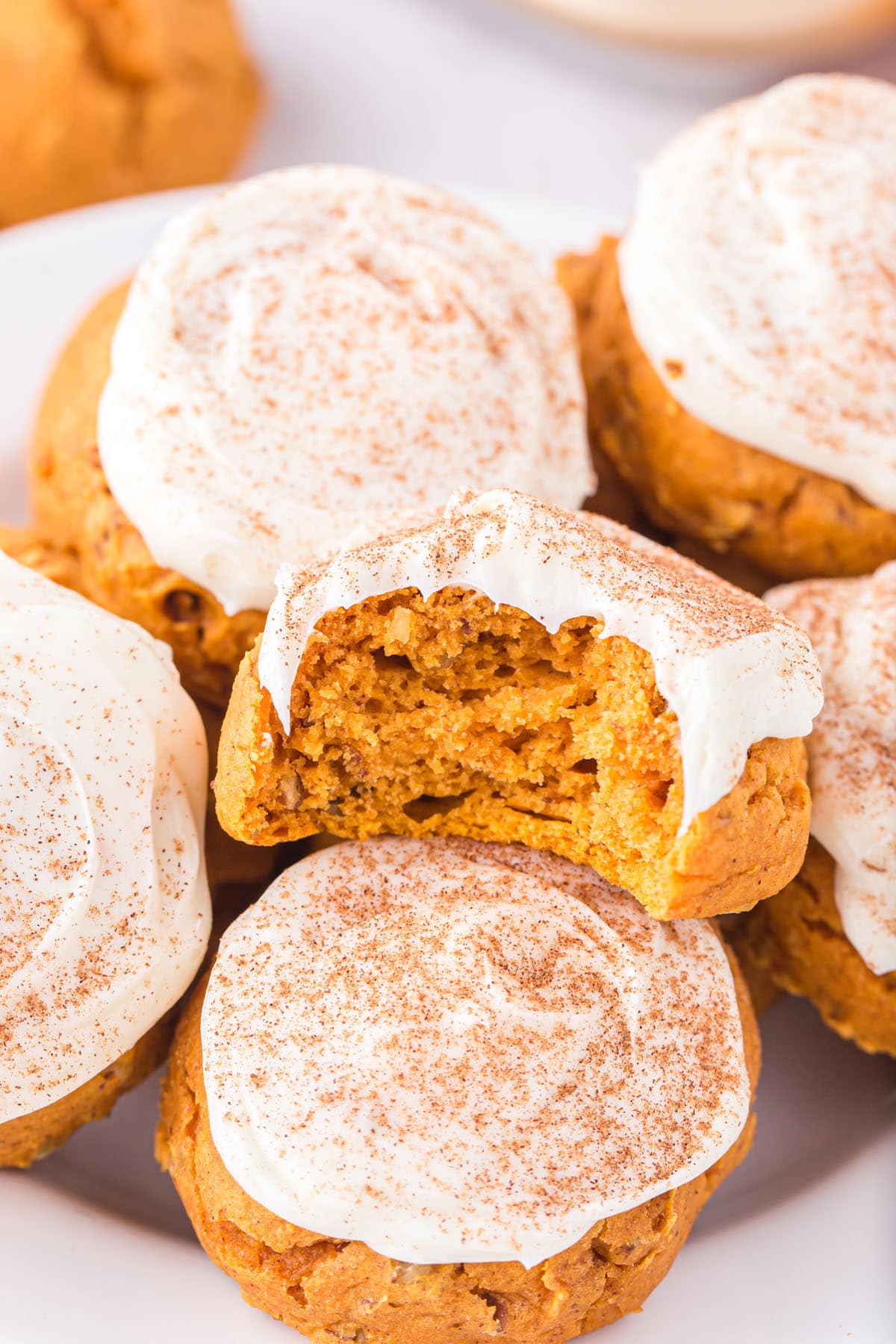 a couple of Pumpkin Cake Mix Cookies on the plate with vanilla frosting and one has a bite taken out.