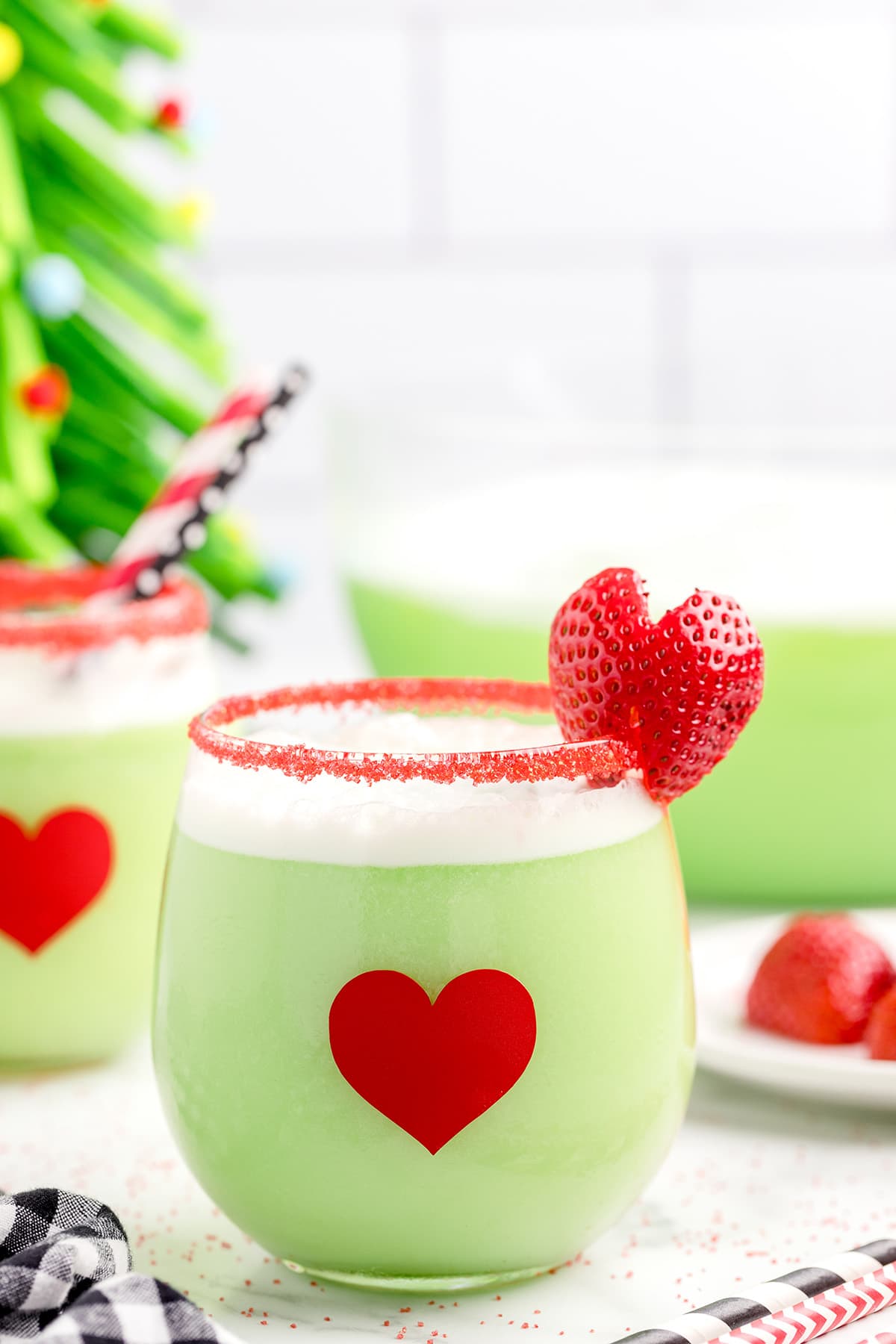 Grinch punch with a red sugar rim and a strawberry on the rim that is cut like a heart