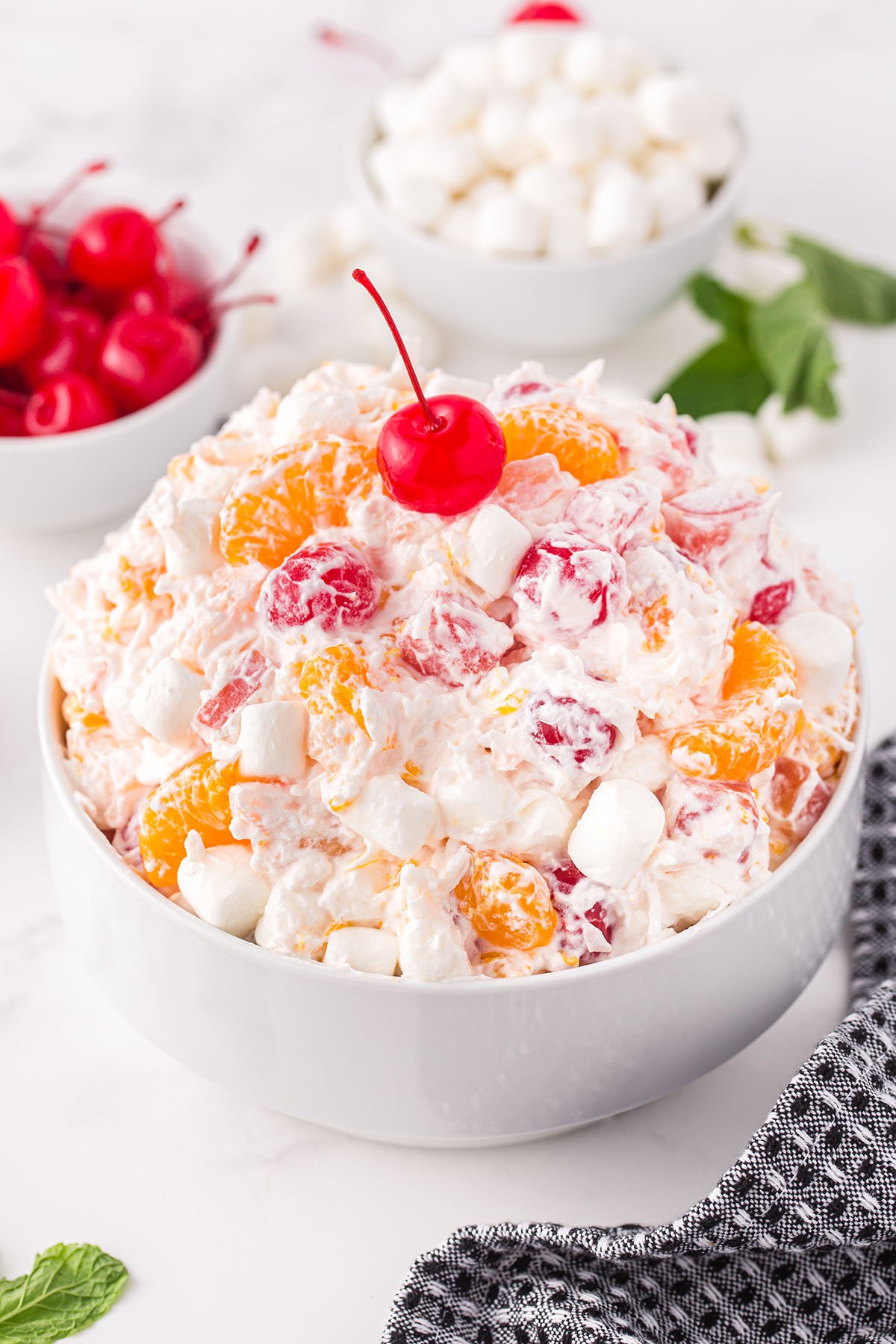 Close up of Ambrosia Salad in a white bowl with a cherry on top 

