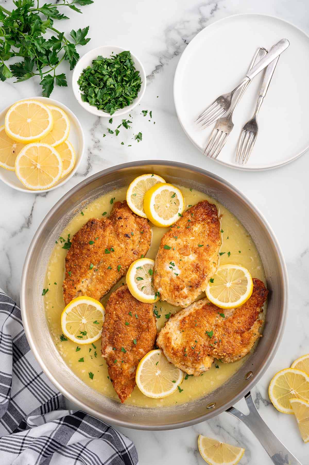 Lemon chicken in a skillet with sauce, garnished with parsley and lemon slices.