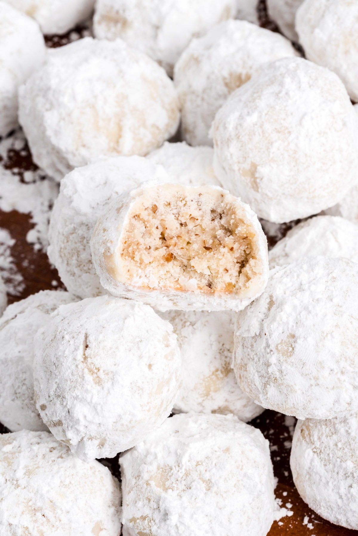 a stack of snowball cookies with one having a bite out of it.