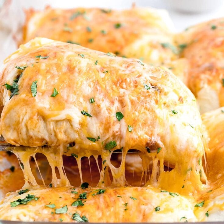 Close-up of a cheesy baked burrito being lifted from a dish, with melted cheese stretching and topped with chopped cilantro.