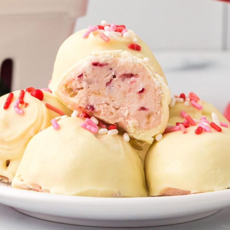 Strawberry Shortcake Truffles on a white plate, one cut open to show pink strawberry filling and pink white sprinkles.
