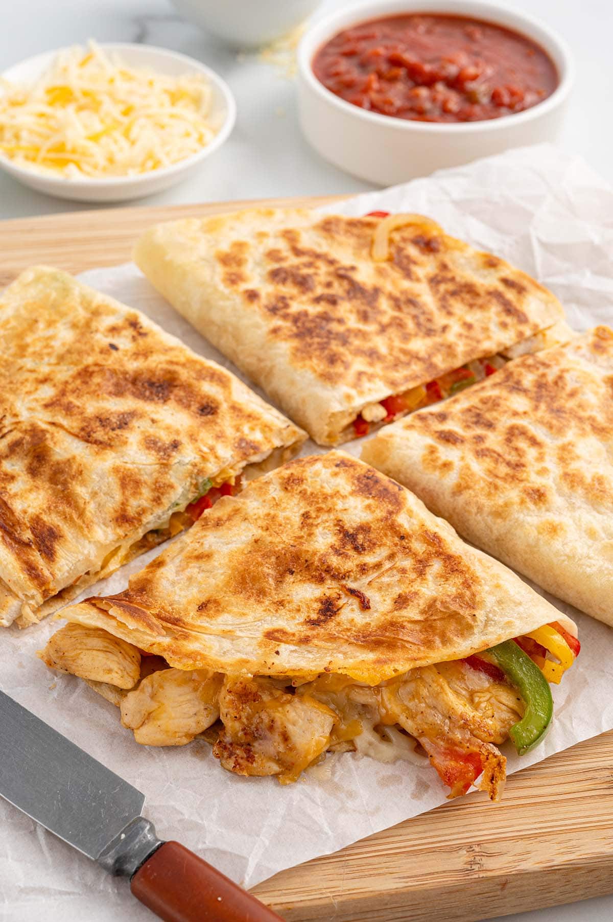 Four slices of fajita quesadilla on top of wooden board.