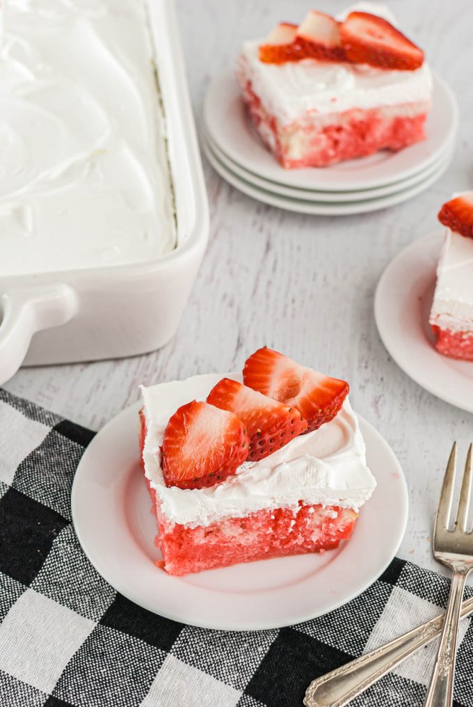 jello poke cake on a white plate with strawberry slices on top.