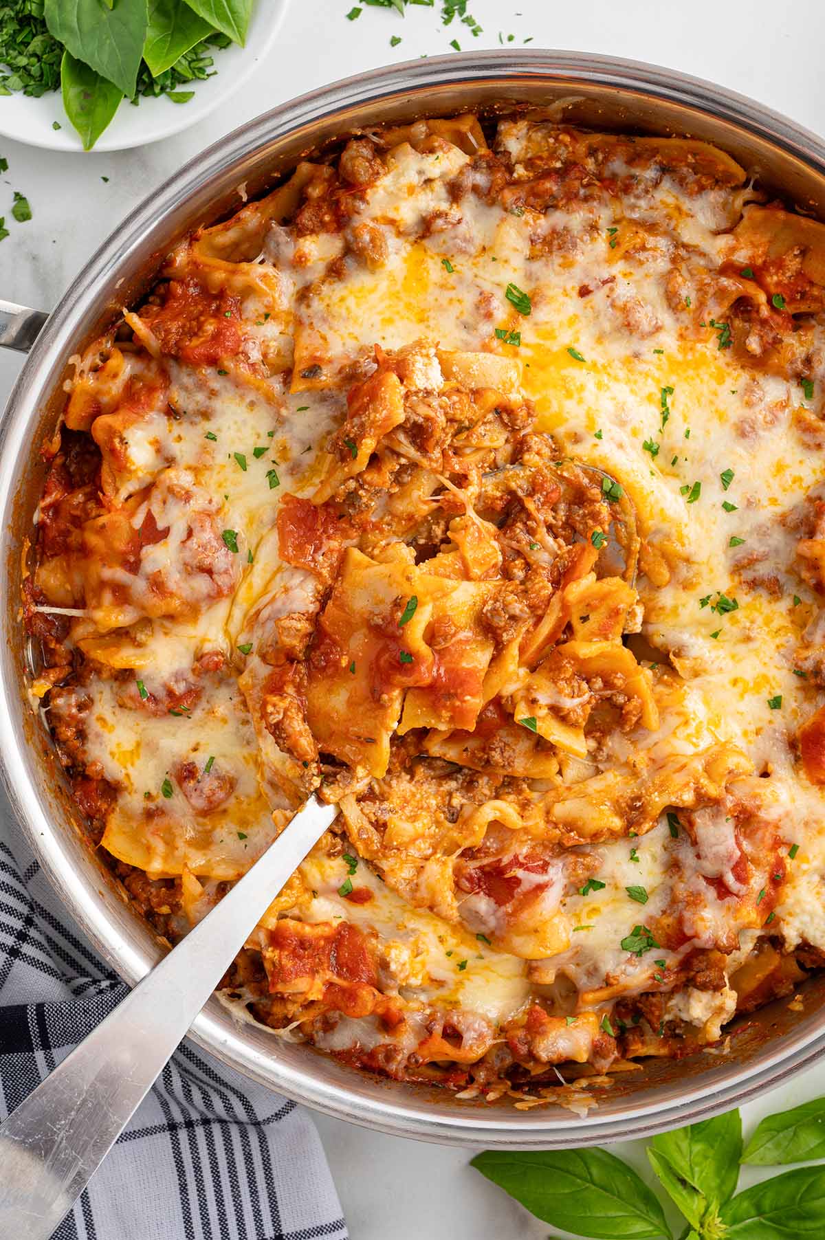 A bubbling skillet of cheesy lasagna topped with fresh herbs.