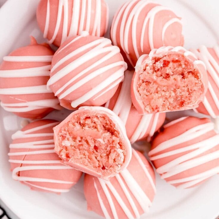 Pink strawberry cheesecake bites with white chocolate drizzle, some with a bite showing creamy filling.