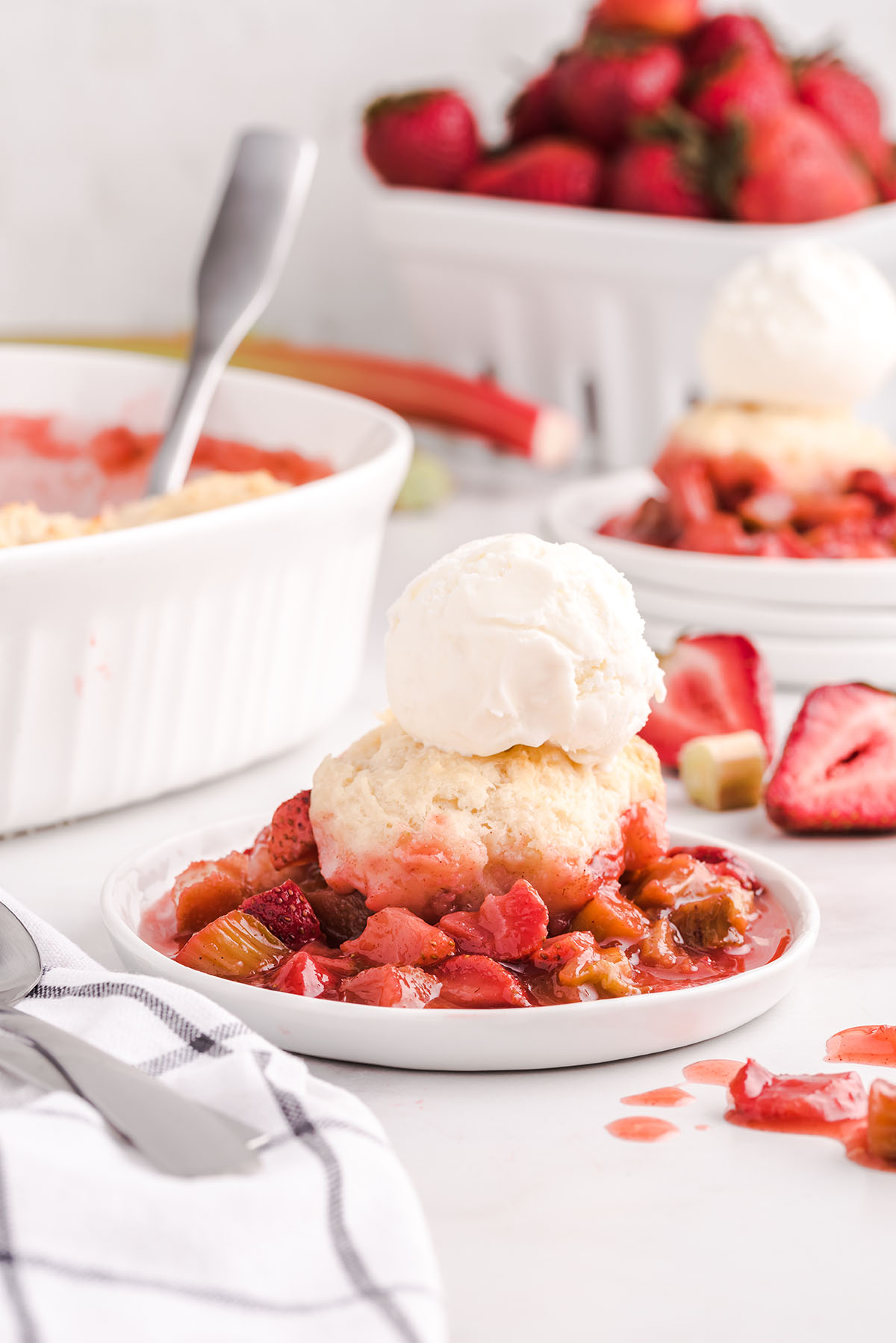 strawberry rhubarb cobbler with ice cream on top on a white plate.