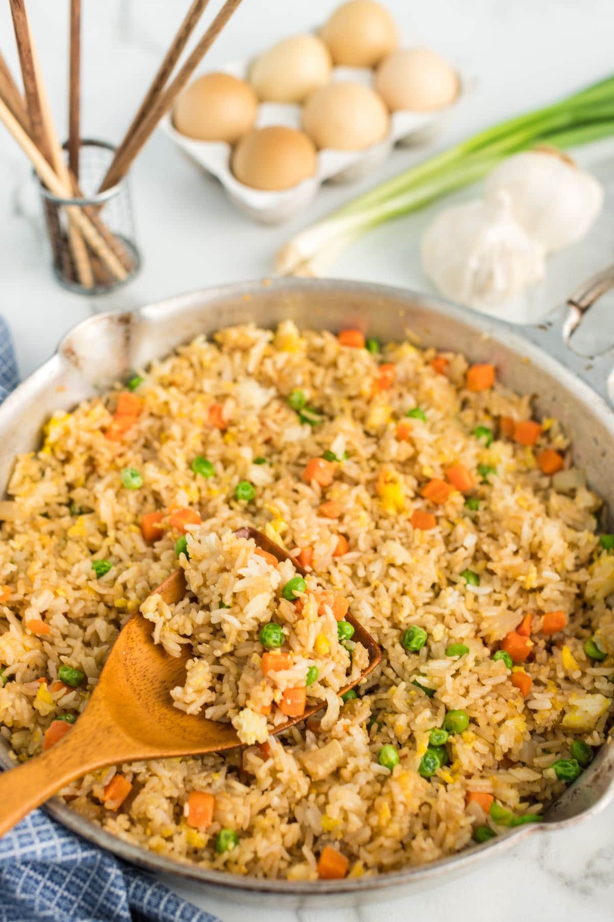 fried rice in a skilet with peas and carrots and a wooden spoon scooping some up.