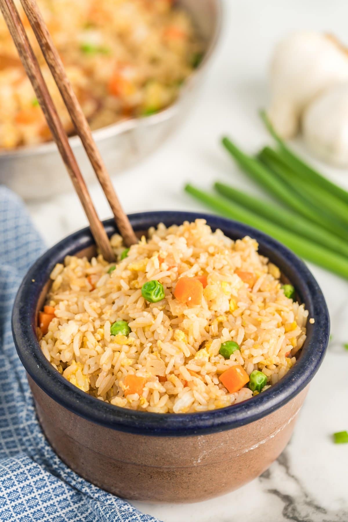fried rice with egg, carrots and peas in a brown bowl with chopsticks.