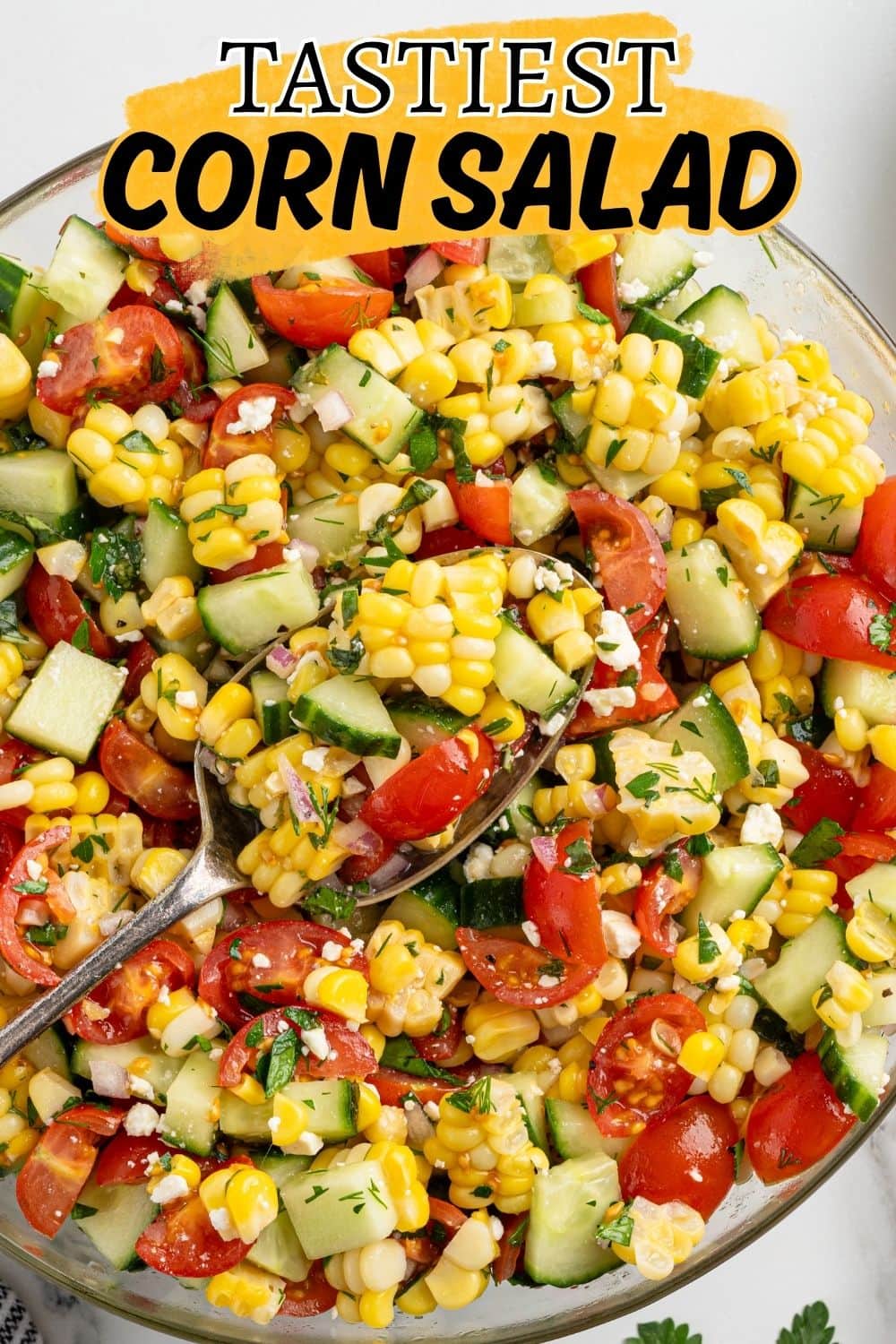 Close-up of fresh corn salad with cherry tomatoes, cucumber, feta, and herbs being served with a spoon.
