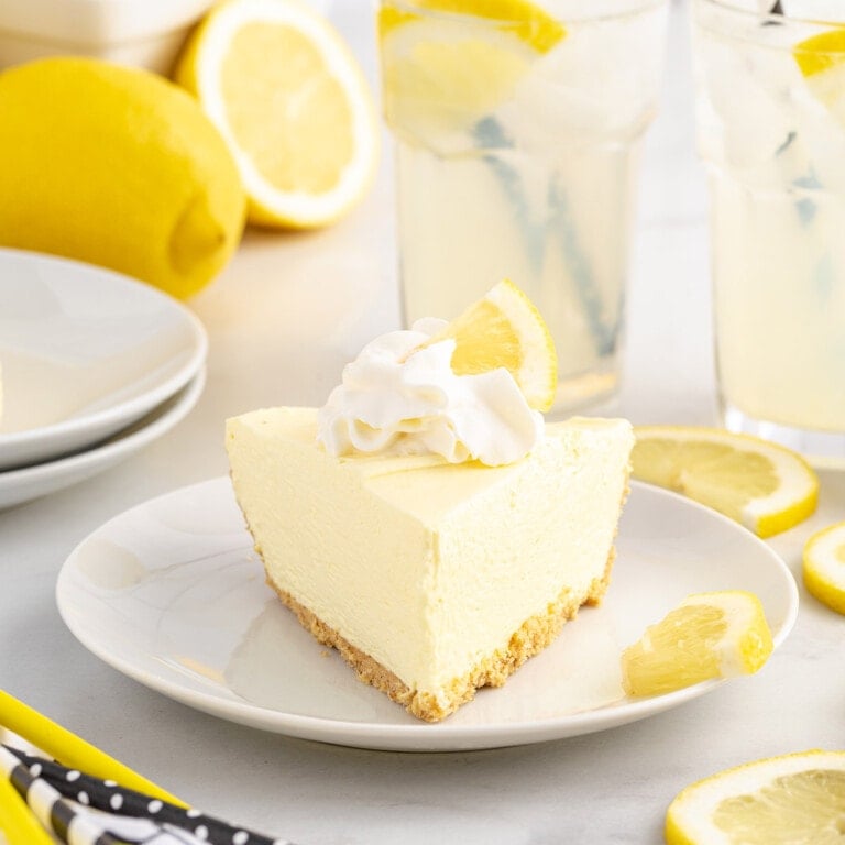A slice of lemonade pie with a graham cracker crust, topped with whipped cream and a lemon slice.