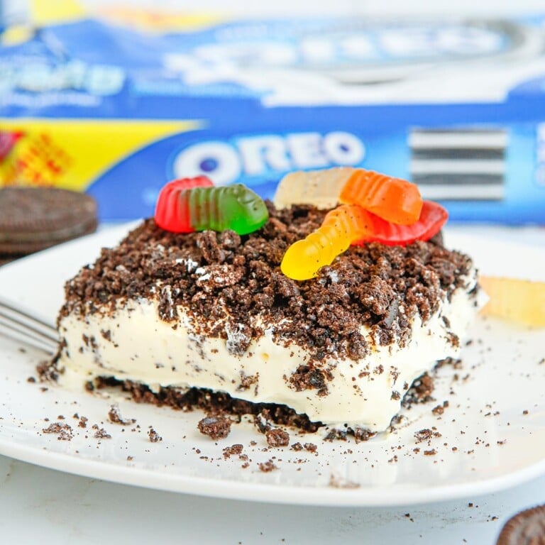 Slice of Oreo dirt cake topped with crushed Oreos and gummy worms on a white plate.