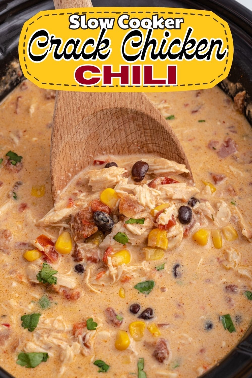 Wooden spoon scooping creamy chicken chili with corn and black beans from a slow cooker.