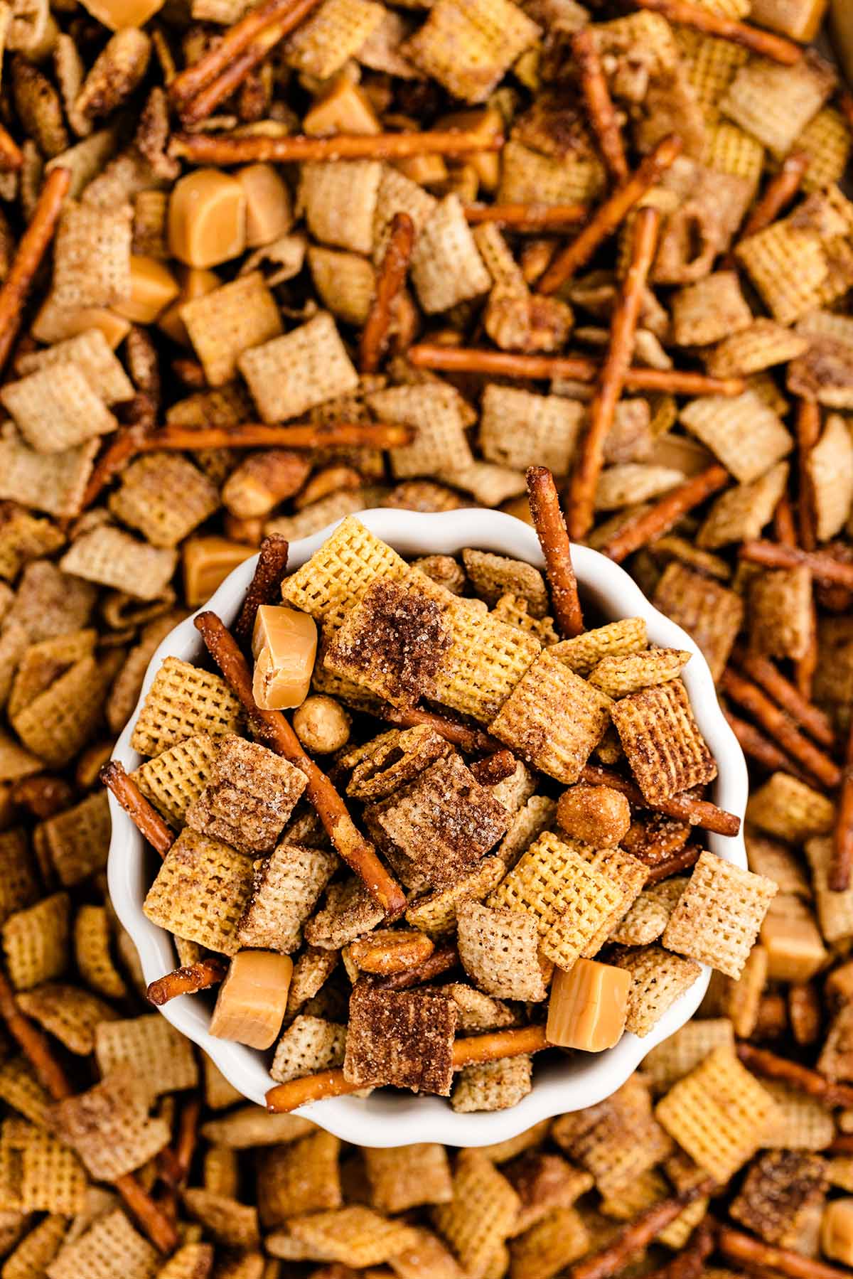 a bowl of churro chex mix in the middle of baking pan full of churro chex mix.
