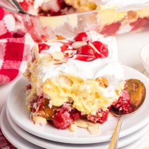 Slice of Heaven on Earth Cake with cherries, whipped topping, pudding, and almond slices on a white plate.