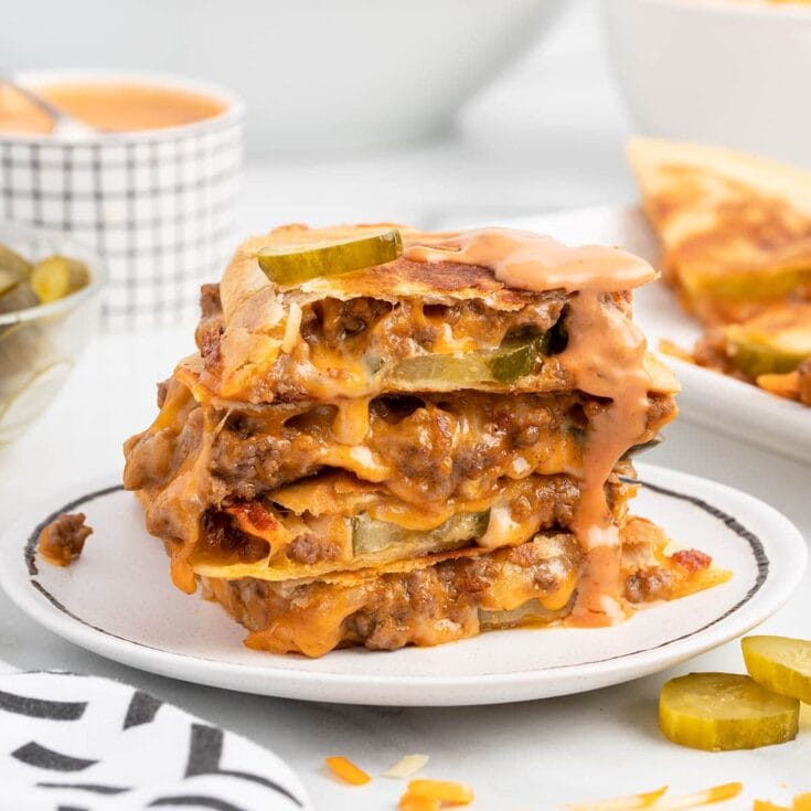Cheeseburger quesadilla stack with melted cheese, ground beef, and pickles on a white plate.