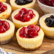 a couple mini cheesecake with topping on top of wooden board.