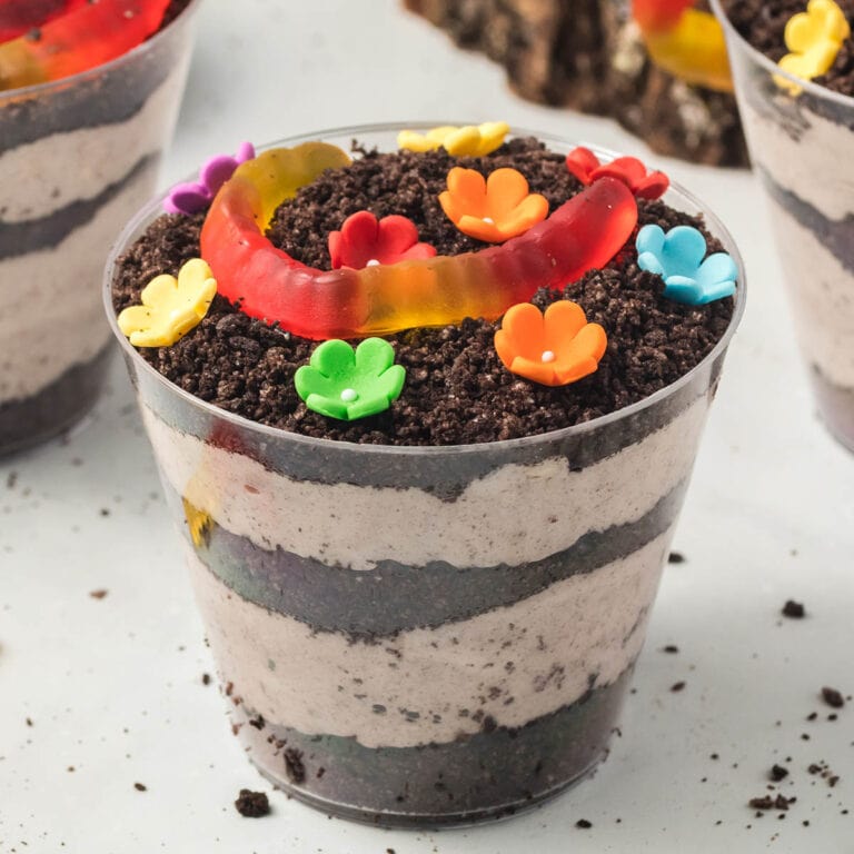 Mini dirt cake cup with Oreo layers, creamy filling, a gummy worm, and candy flowers.