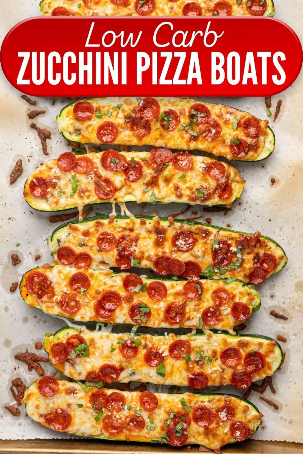 Low Carb Zucchini Pizza Boats with melted cheese, mini pepperoni, and fresh basil on a parchment-lined baking sheet.