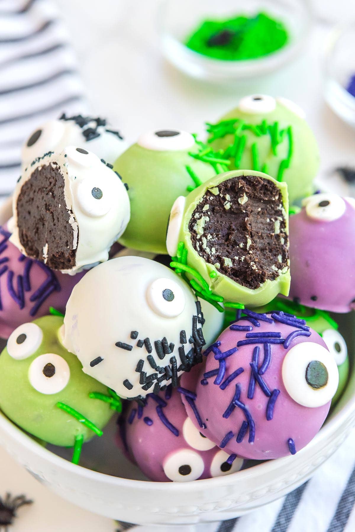 bitten oreo balls with green candy coating in a bowl together with a couple more monster eye balls.