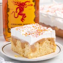 a slice of Fireball Poke Cake on a white place with fireball bottle on the background