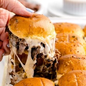 taking a piece of french dip sliders from casserole dish