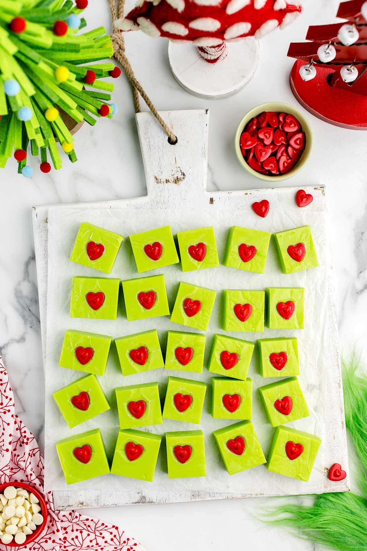 a couple of Grinch Fudge with red heart candies on a wooden board.