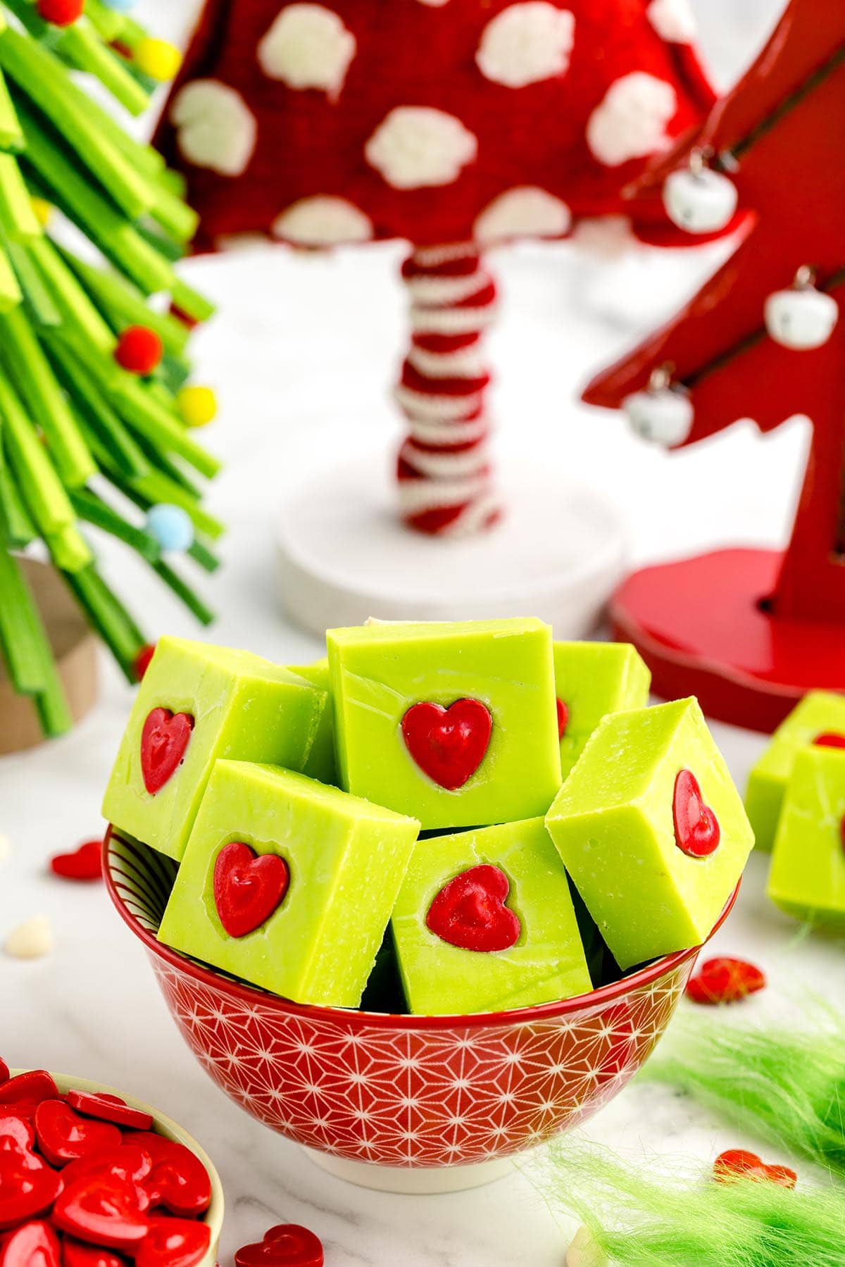 Grinch Fudge in a bowl with red heart candies and some Christmas tree on the background.