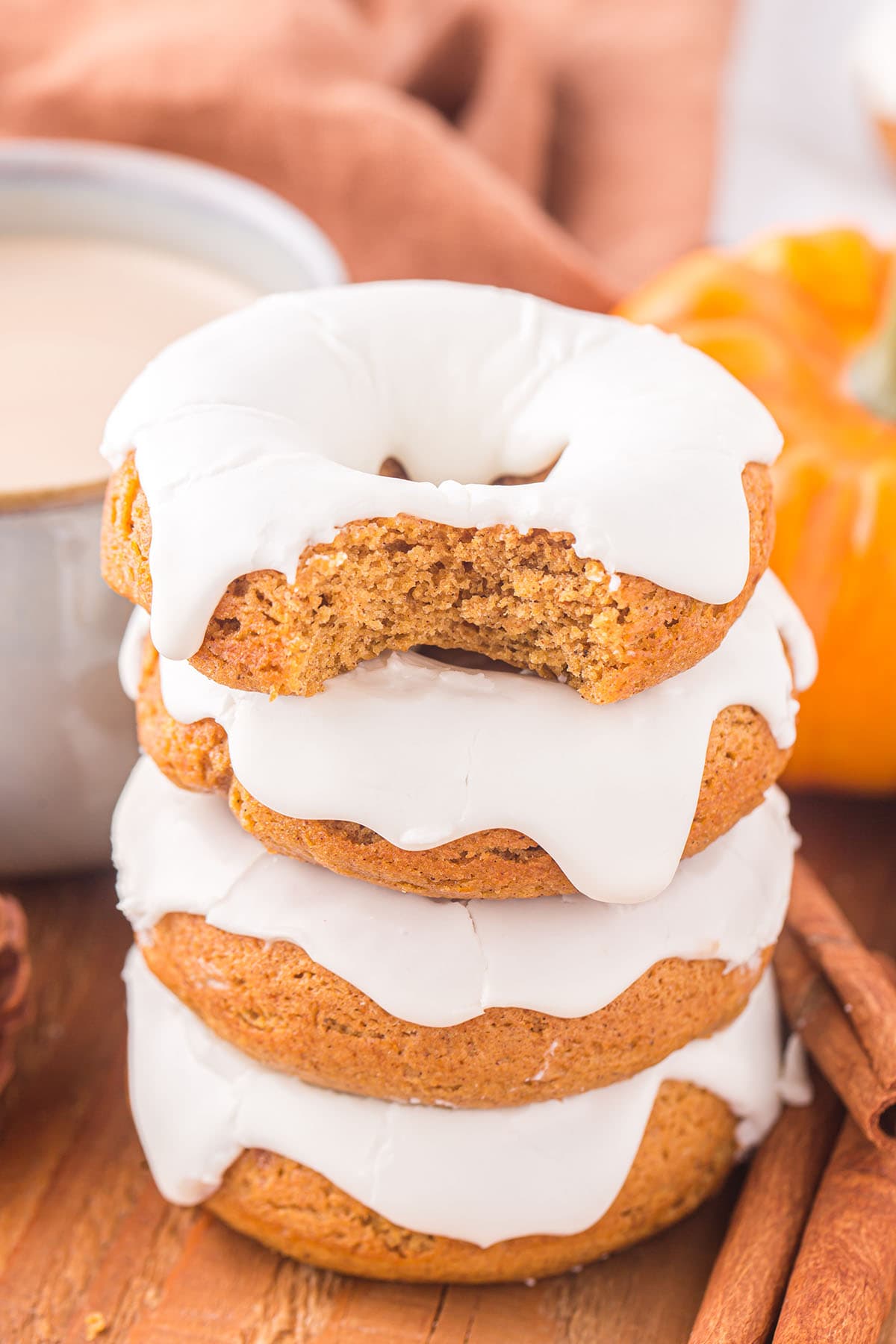 Pumpkin Donuts stacked with white frosting and a bite out of the top one.