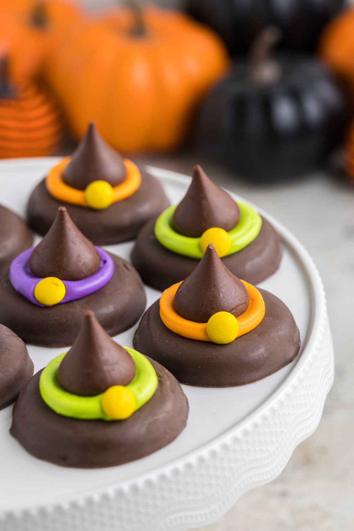 a couple of witch hat cookies on a white serving tray with a couple pumpkins on the background.