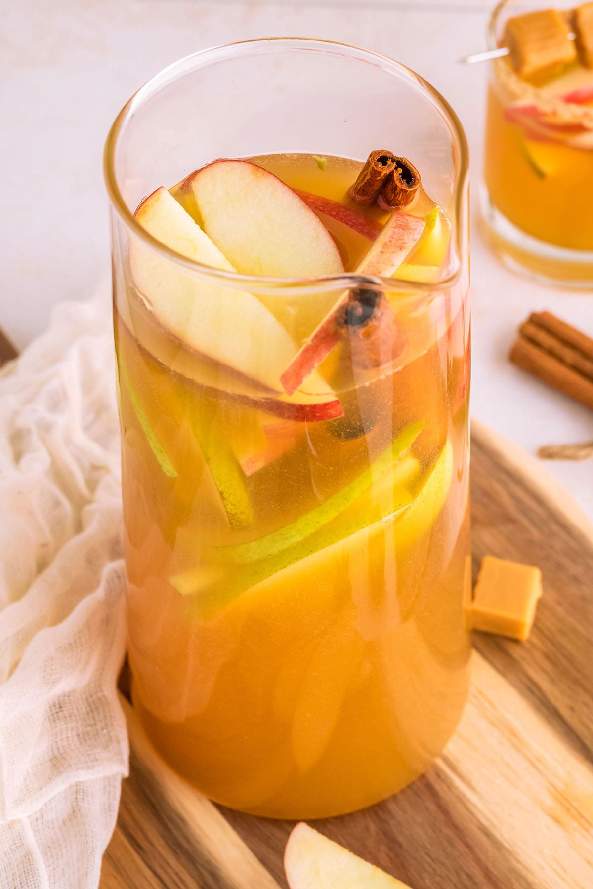 caramel apple sangria in a glass pitcher with pears and apples floating on top.