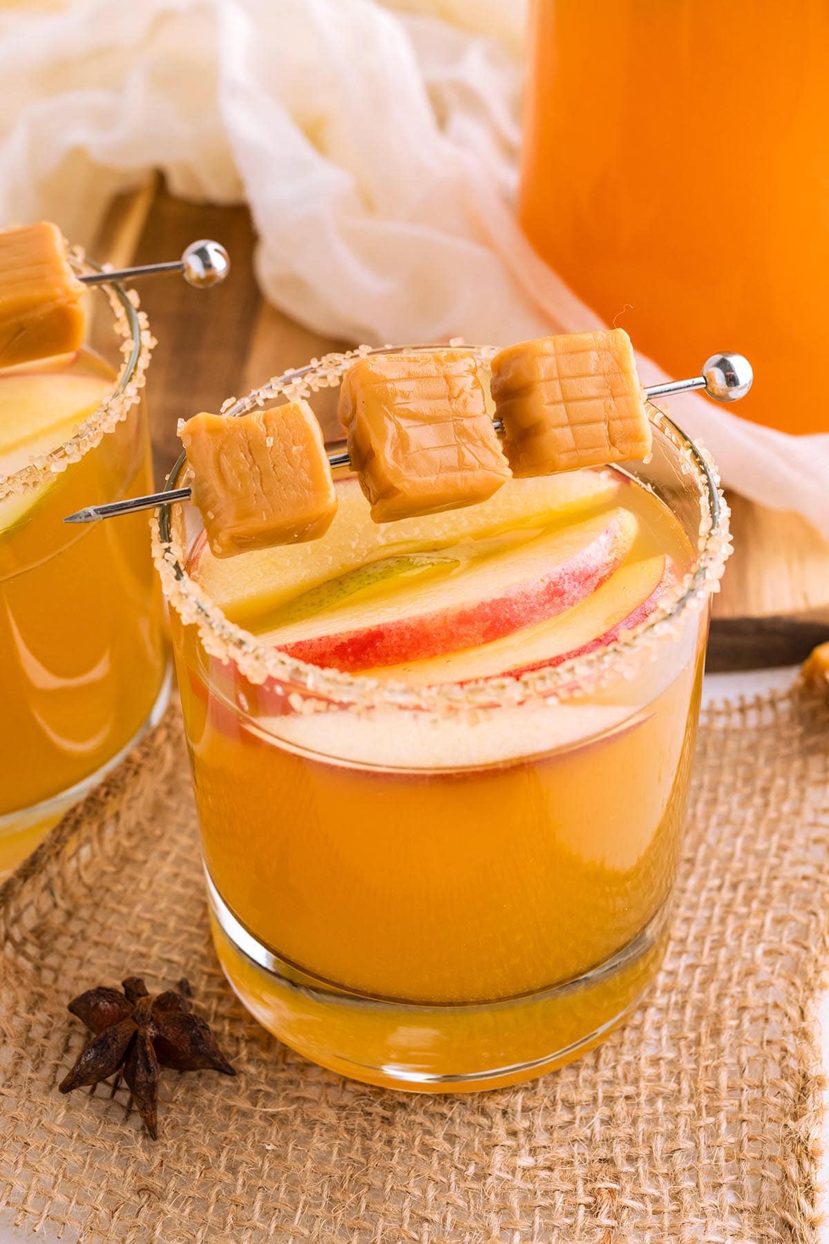 a glass of caramel apple sangria with a cinnamon sugar rim and apples floating on top with 3 caramels on top.