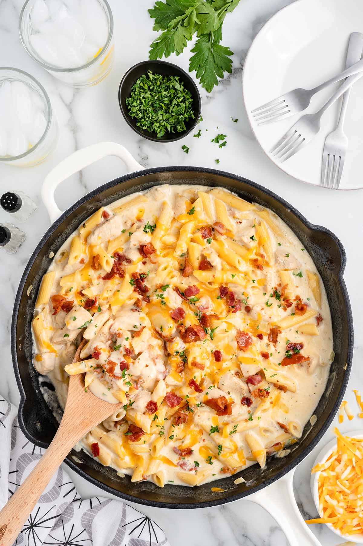 Crack Chicken Penne on a white table with parsley and cheese on the side.