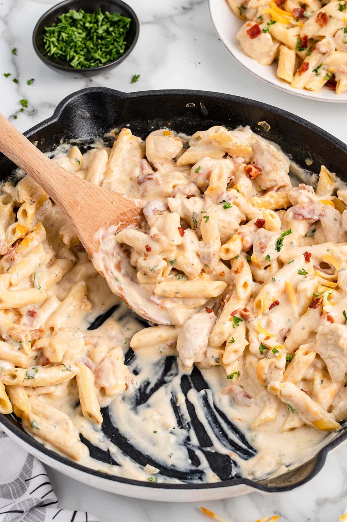 scooping Crack Chicken Penne on a skillet using a wooden spoon.