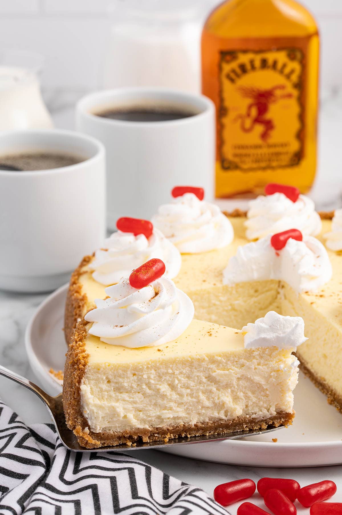 cutting a triangle piece of Fireball Cheesecake with 2 glasses of coffee on the background.