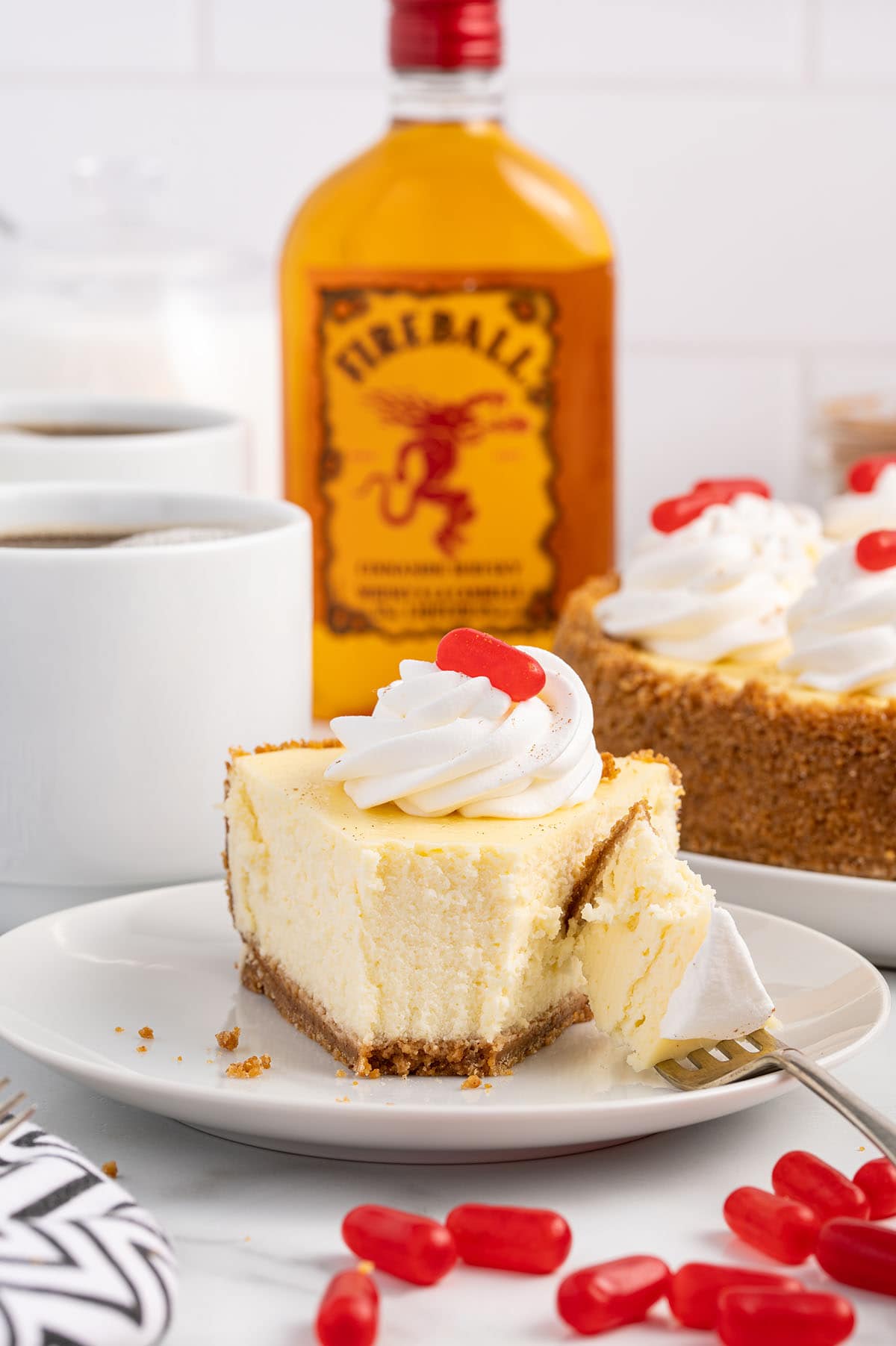 a triangle slice of Fireball Cheesecake with Fireball bottle on the background.