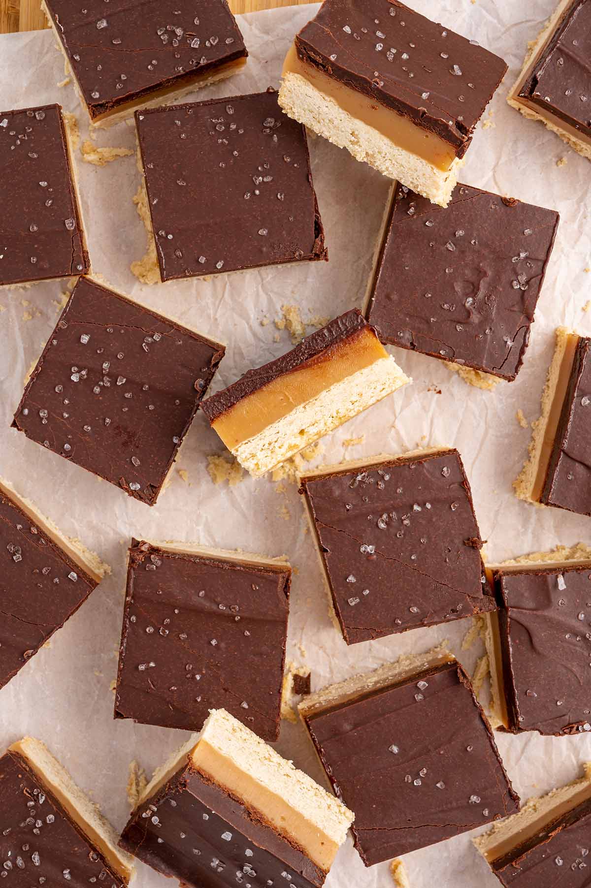Millionaire Shortbread cut into squares and scattered around on top of parchment paper.