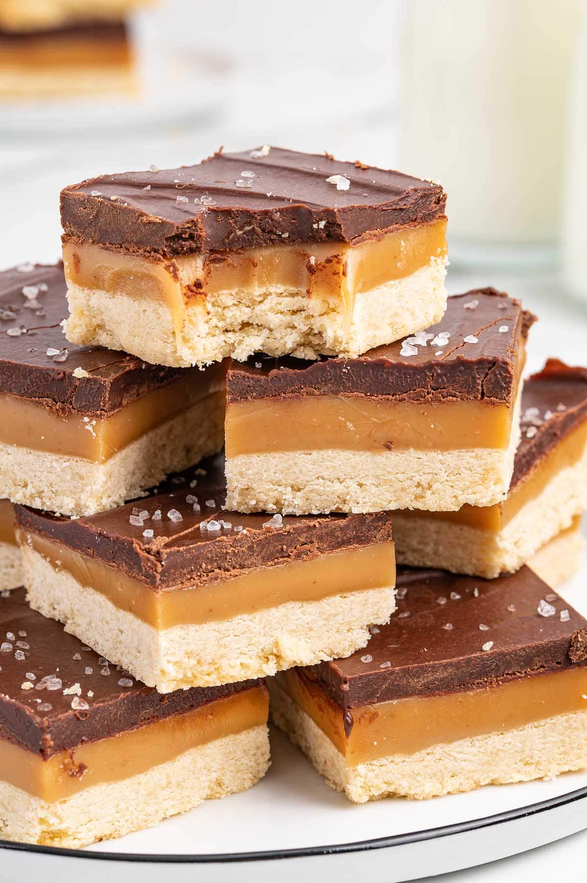 a couple pieces of millionaire shortbread stacked on top of each other - on with a bite taken out.