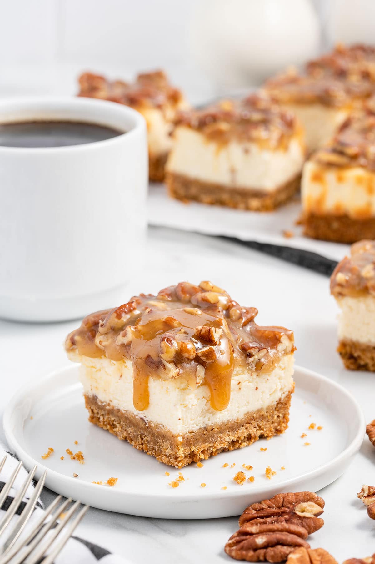 Pecan Pie Cheesecake Bars on a white plate and a cup of coffee at the background.