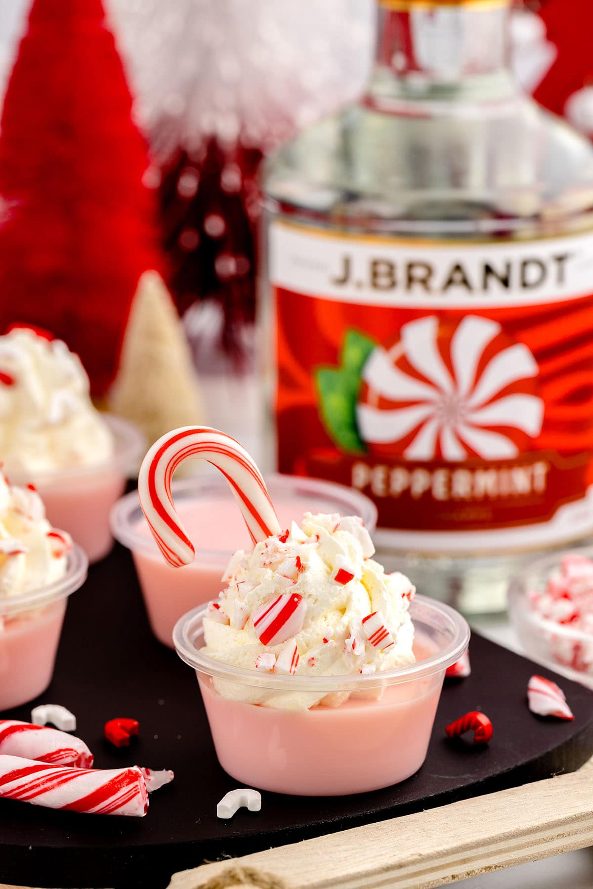 Candy Cane Jello Shots in a small plastic cups with a bottle of alcohol on the background.