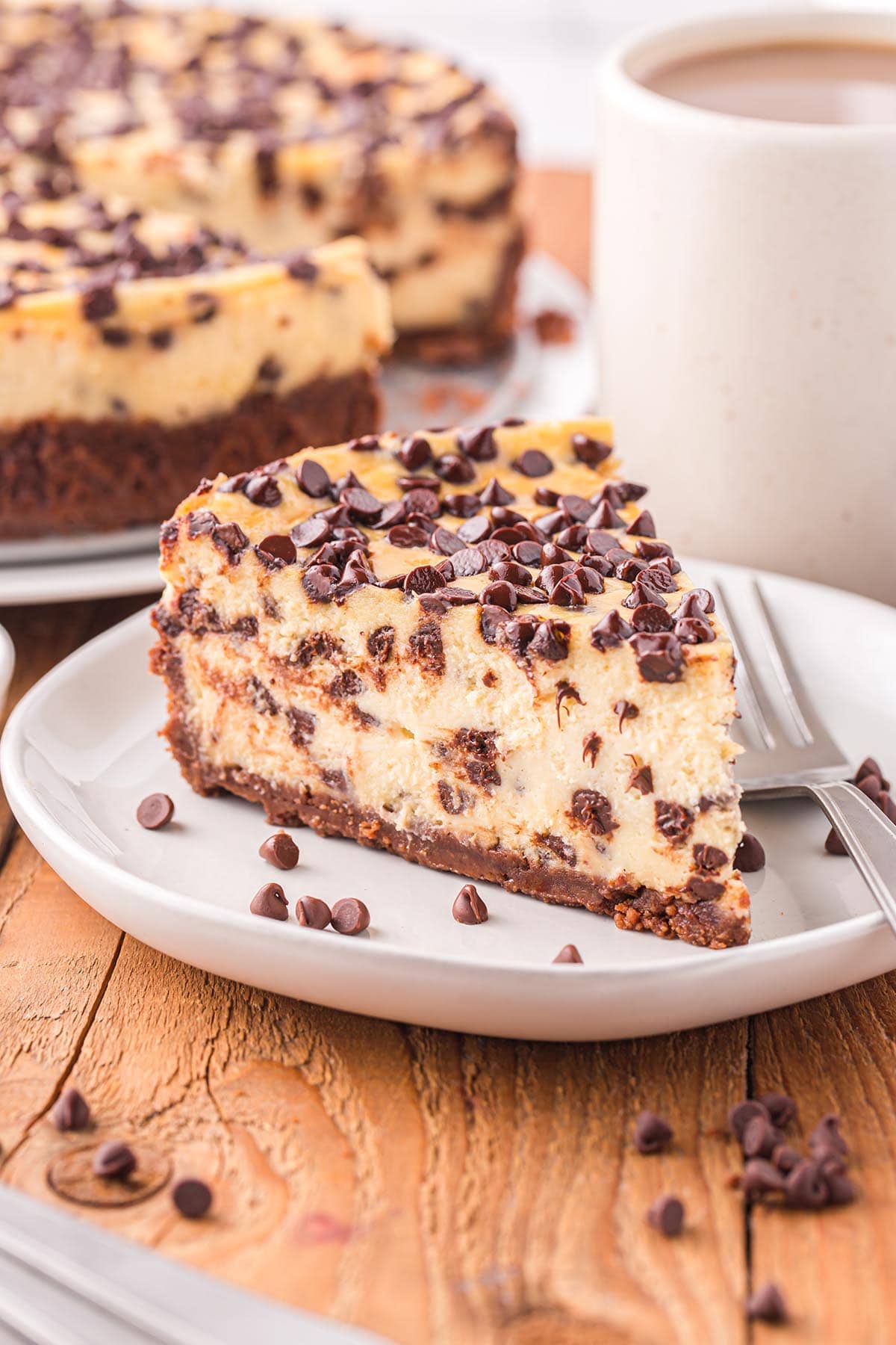 Chocolate Chip Cheesecake sliced on a white plate with a mug of coffee at the back.